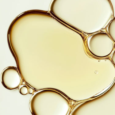 Aceite corporal de incienso y mirra de ALQVIMIA: Detalle ampliado de gotas de aceite de tonalidad dorada.