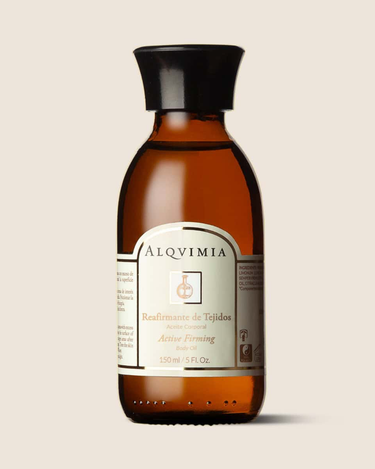 Aceite corporal reafirmante de ALQVIMIA: frasco ámbar con tapón negro, sobre fondo beige.