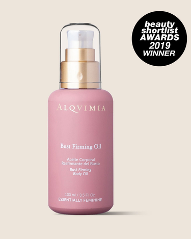 Aceite reafirmante de busto de ALQVIMIA: frasco rosa con dosificador dorado, sobre fondo beige.