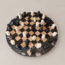 Ajedrez de piedra con tablero circular y piezas claras y oscuras distribuidas sobre el damero.