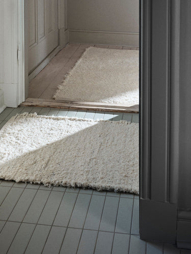Alfombra de algodón blanco roto junto a una puerta de madera