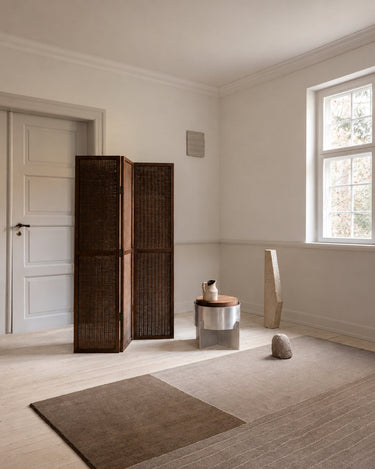 Hand-knotted moss green wool rug by Linie Design, in perspective beside a wooden screen