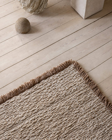 Beige wool rug with a fringed border by Linie Design, edge detail beside a stone object