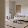 Beige wool rug with a fringed border by Linie Design, in a living room with a white sofa