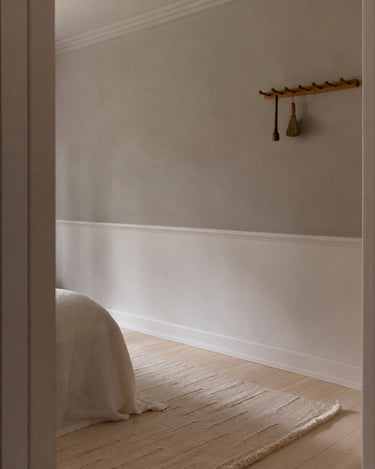 Beige wool rug with wavy lines by Linie Design, at the foot of a bed