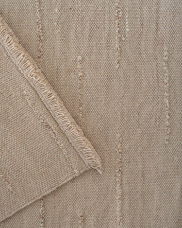 Beige wool rug with wavy lines by Linie Design, folded corner revealing the weave