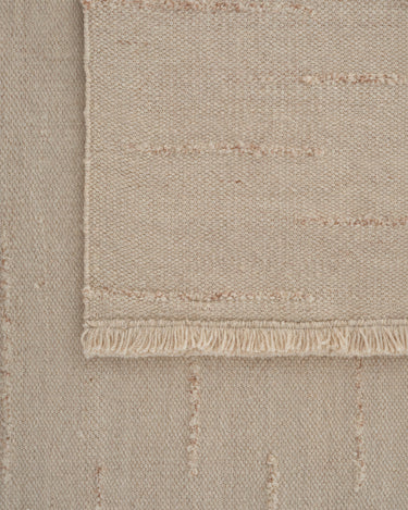 Beige wool rug with wavy lines by Linie Design, close view of an end with fringes