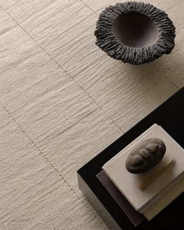 Cream jute rug with an open weave by Linie Design, beside a table and dark bowl