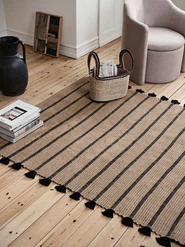 Alfombra Ezra natural y negra bajo un sofá