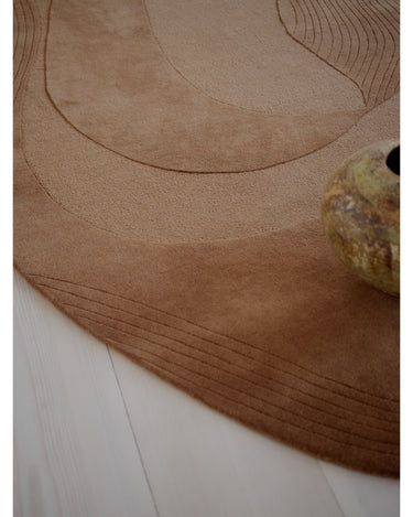 Alfombra irregular de lana ámbar con relieve de Linie Design: detalle de la superficie con un jarrón.