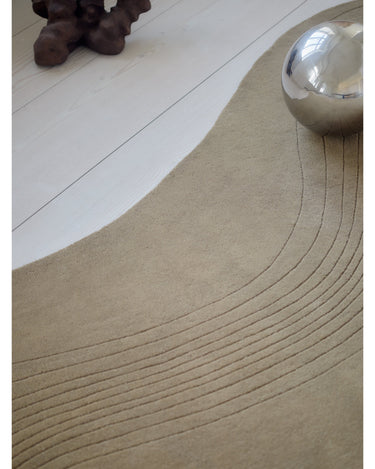 Alfombra irregular de lana verde oliva con surcos de Linie Design: detalle de los surcos junto a un jarrón.