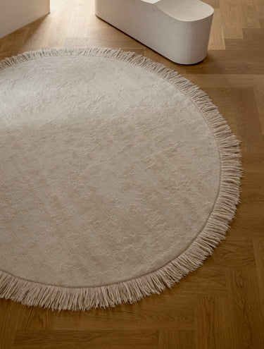 Alfombra irregular y redonda de lana beige Oceanic Reef de Linie Design, extendida sobre suelo de madera