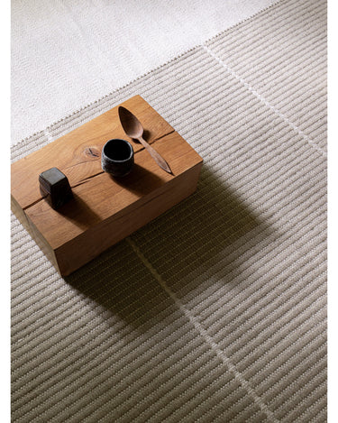 Alfombra de lana beige con cuadrícula tejida de Linie Design: vista oblicua junto a una mesa baja.