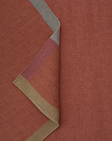 Pli du tapis en laine terracotta montrant son revers et ses bordures colorées