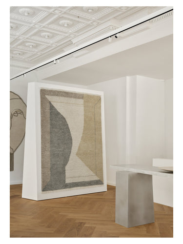 Alfombra de lana con diseño óptico Optical Echo de Linie Design, expuesta verticalmente junto a un pedestal