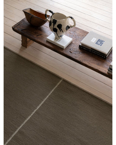 Alfombra de lana y lino verde con línea central de Linie Design: detalle de la línea junto a una mesa.