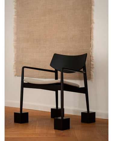 Alfombra de lana marfil con flecos de lino de Linie Design: vista de ambiente junto a una silla oscura.