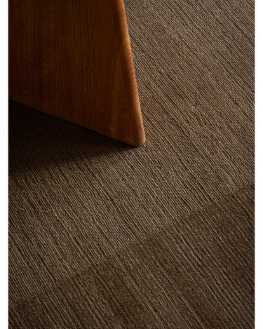 Alfombra de lana marrón oliva de dos texturas de Linie Design: detalle de la textura junto a una pata de madera.