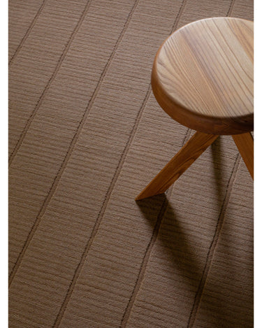 Alfombra de Linie Design: detalle de la cuadrícula junto a un taburete.