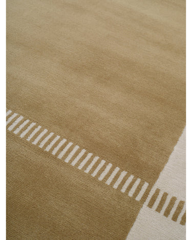 Alfombra de lana ocre con dibujo geométrico de Linie Design: detalle de la banda clara junto a un asiento.
