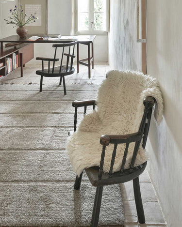 Alfombra lavable de lana orgánica blanca con forma de piel junto a una cama