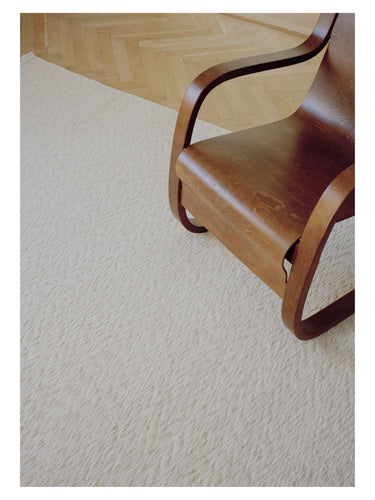 Alfombra de lana trenzada Blonde Maze de Linie Design, superficie junto a una silla de madera