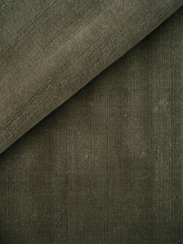 Alfombra de lana verde musgo con bordes bouclé Halo Cloud de Linie Design, detalle del pelo verde con una esquina doblada