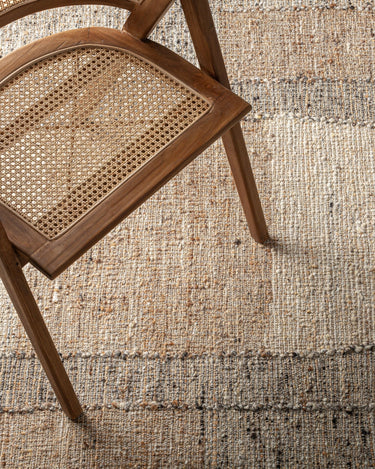 Alfombra de lana yute algodón tonos neutros de Vical, alfombra de franjas en tonos neutros bajo una silla de madera