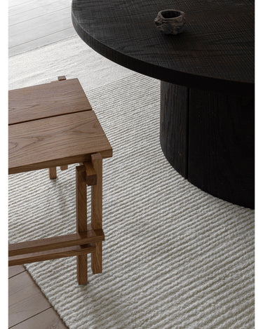 Alfombra de lino beige con extremos en contraste de Linie Design: detalle junto a una mesa y un asiento.