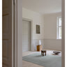 Alfombra de lino gris menta con líneas orgánicas de Linie Design: en una estancia clara con taburete de madera.