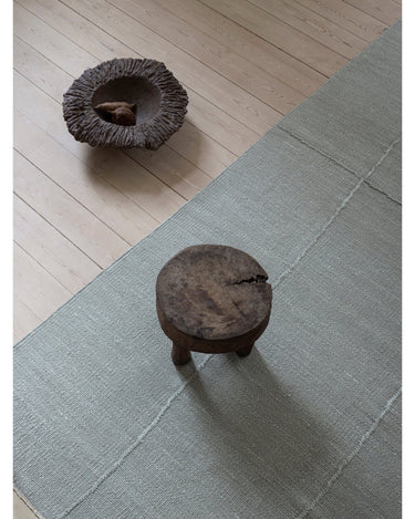 Alfombra de lino gris menta con líneas orgánicas de Linie Design: vista oblicua sobre suelo de madera.