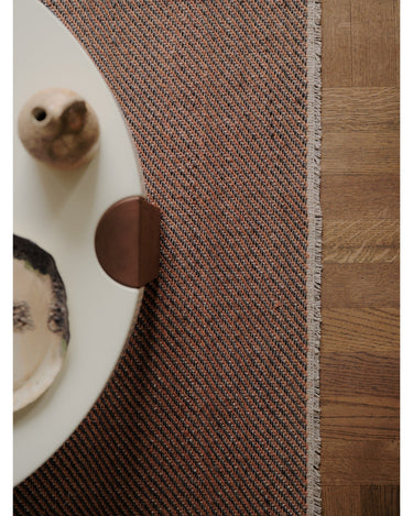Alfombra de lino y sisal color óxido de Linie Design: detalle del borde junto a la mesa.
