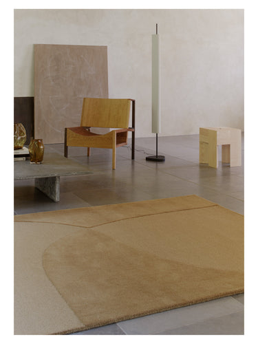 Alfombra mostaza de lana Split Plains de Linie Design, junto a un sillón de madera