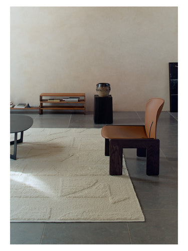 Alfombra Polar Angels blanca de Linie Design, junto a una mesa baja y un sillón