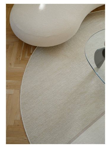 Alfombra redonda beige Magnetize de Linie Design, detalle del borde junto a un sofá curvo
