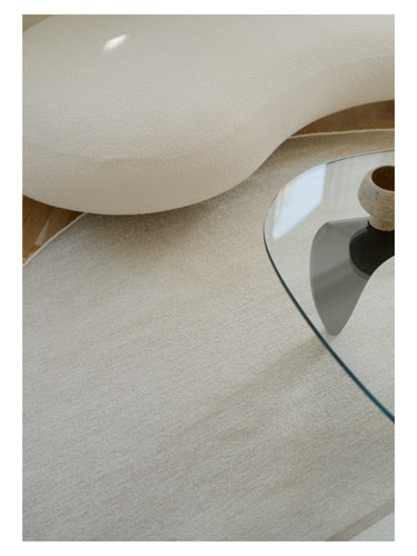 Alfombra redonda beige Magnetize de Linie Design, detalle de la superficie junto a una mesa de vidrio