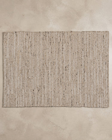 Alfombra Vical de lana y algodón beige sobre superficie topo clara texturizada