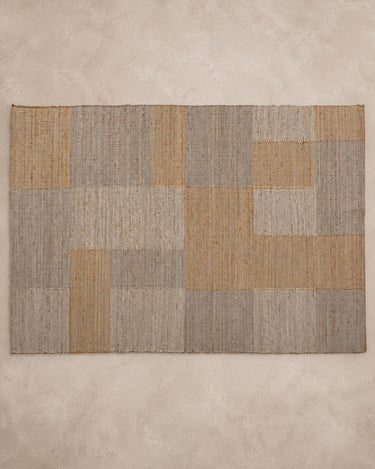 Alfombra Vical de yute y algodón gris y ocre sobre superficie topo clara texturizada