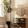 Aparador de acero negro con cristal estriado de Ferm Living: aparador de dos puertas de cristal bajo espejo redondo, con planta a un lado y objetos dentro.