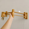 Aplique de madera con brazos extensibles, soporte mural y portalámparas sin pantalla.