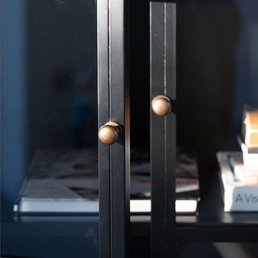 Armario alto de metal negro con puertas de cristal en una composición de Tine K Home
