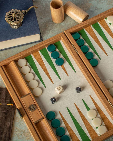 Backgammon de Manopoulos: vista próxima del tablero con dados y cubiletes junto a libro y objeto decorativo.