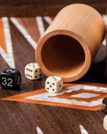 Cubilete de madera tumbado con dados sobre el tablero.