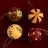 Bolas de Navidad de papel maché en tonos rojos de Mahe Homeware, con dibujos crema y acentos verdes.