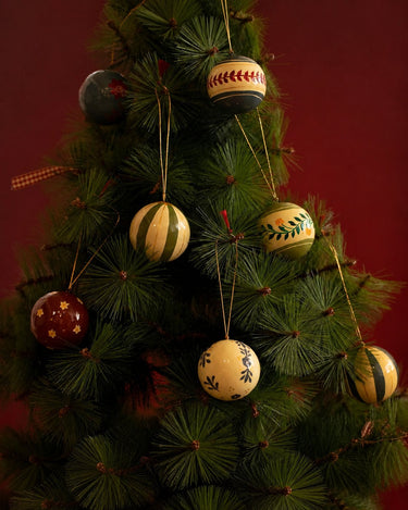 Bolas de Navidad de papel maché de varios colores colgadas entre las ramas del árbol.