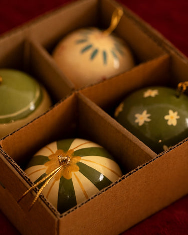 Juego de cuatro bolas navideñas verdes y crema colocado en su caja.