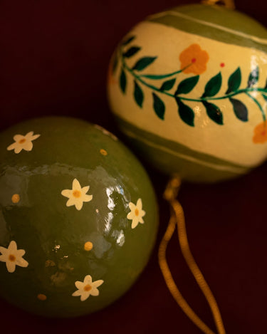 Detalle de una bola verde de papel maché con una flor pintada a mano.
