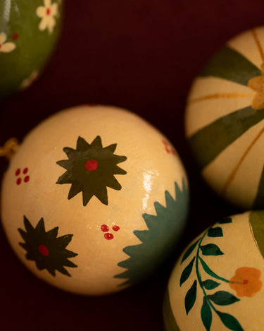 Bolas de Navidad de Mahe Homeware: primer plano de un adorno crema con motivos verdes pintados.