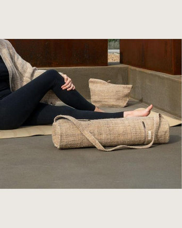 Bolsa de cáñamo para esterilla de yoga de Bed and Philosophy, junto a una esterilla y una persona sentada