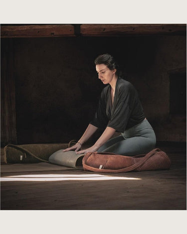 Bolsa para esterilla de yoga de pana canela de Bed and Philosophy junto a una persona y una esterilla